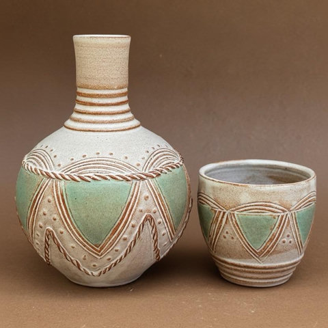 The same object but in this photo, the cup sits next to the bottle reveling the bottle’s tall slender neck. The cup and the bottle are decorated to match each other—with aqua triangle accents and decorative rings around the neck of the vase and the foot of the cup. 