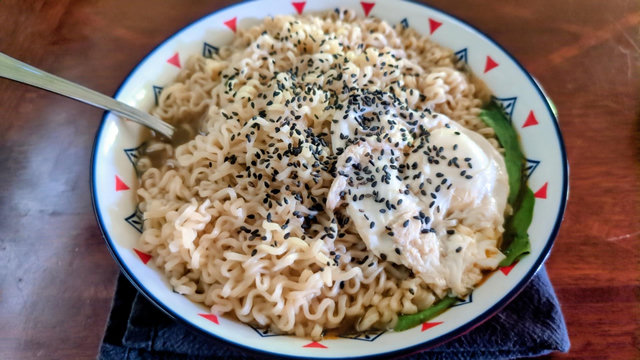 A close photo of a large bowl of ramen. Spinach and a seasoned egg decorate the tan noodles, with black sesame seeds garnishing the top.