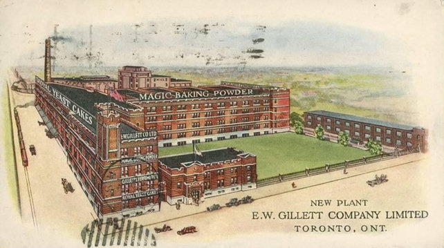 A postcard from 1910s depicting the EW Gillett company complex in Liberty Village, Toronto. An illustration of a block of brick buildings, one of them has a tall chimney, one of them reads “Magic Baking Powder” and the other “Royal Yeast Cakes”. On the left there is a little train (way too small for the size of the building but there used to be train tracks there) and some very tiny cars. I want a print of this