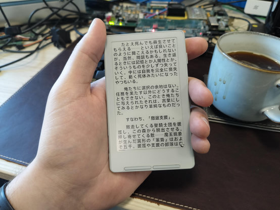 Palm sized e reader with Japanese text. Coffee mug and FPGA board in the background