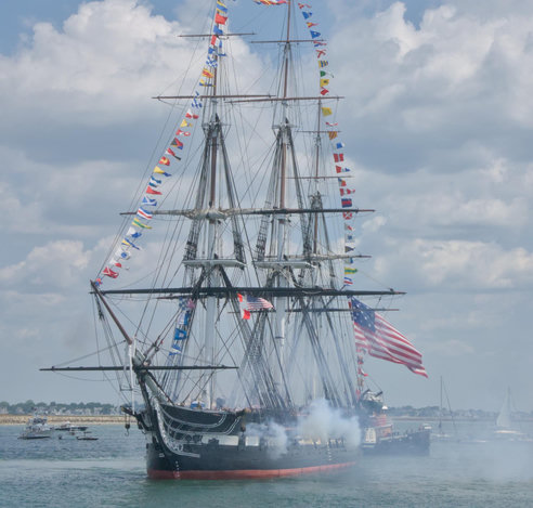 The USS Constitution, firing its guns in salute off the shore of Castle Island
