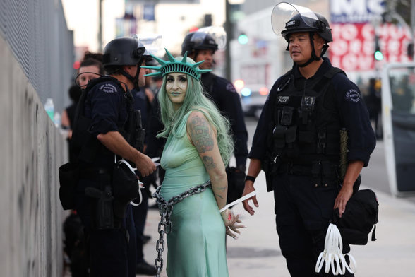 Woman dressed up as the statue of liberty looking at the camera while being arrested surrounding by cops in Portland during No Kings protests