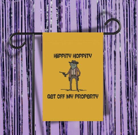 A yellow garden flag on a stand, featuring an illustration of a frog dressed as a cowboy holding a gun, with the text "HIPPITY HOPPITY GET OFF MY PROPERTY".