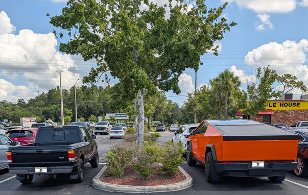 A sensible (old) black Ford Ranger on the left and a ridiculous orange CyberTruck on the left, in a parking lot in Wesley Chapel, Florida, where I was buying glue at the closest hardware store, a mere 7 miles from my late father-in-law's home.