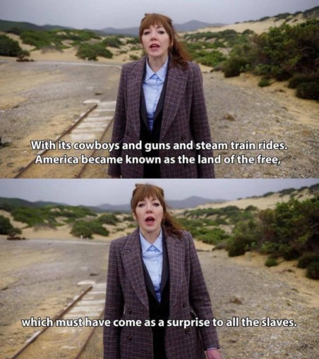 A two-panel image macro featuring Philomena Cunk (played by Diane Morgan) standing outdoors in a sandy, coastal landscape with sparse green bushes and old train tracks on the left. She has auburn hair with bangs, pulled back, and is wearing a light blue button-down shirt under a dark vest and a brown plaid blazer.

Top Panel: She looks directly forward with a neutral expression. White text at the bottom reads: "With its cowboys and guns and steam train rides. America became known as the land of the free,"

Bottom Panel: Her mouth is slightly open mid-speech, maintaining a serious expression. White text at the bottom reads: "which must have come as a surprise to all the slaves."