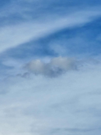 A blue sky streaked with white clouds except this one kind of heart shaped darker cloud with hints of yellow-peach.