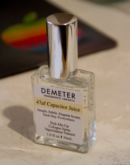 A photo of a bottle of a Demeter fragrance on a desk, with an Apple mouse pad behind. This one is the scent '47uf Capacitor Juice".