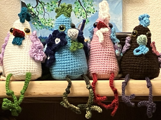 Four crazy crocheted chickens sitting together. White, blue, pink and brown.
