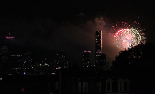 Fireworks against the Boston skyline. The Pru is visible on the left side of the image, and the very top of the Hancock building is just visible over some trees on the right. Red and green fireworks bursts that aren't *quite* in focus illuminate a skyscraper