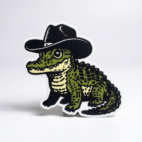 A sticker of a cute, green cartoon alligator wearing a black cowboy hat