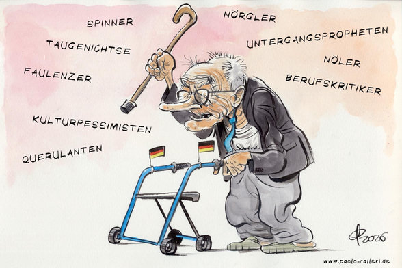 Karikatur "Motivationsredner" aus dem Jahr 2026. Ein Greis mit spärlichem Haarbüschel an der Stirn und langer Nase steht an einem Rollator und schwingt seinen Gehstock. Mehrer Begriffe umschwirren ihn. Spinner, Nörgler, Taugenichtse, Faulenzer, Nöler, Untergangspropheten, Kulturpessimisten, Querulanten, Berufskritiker. Am Rollator sind zwei Deutschlandfähnchen angebracht.