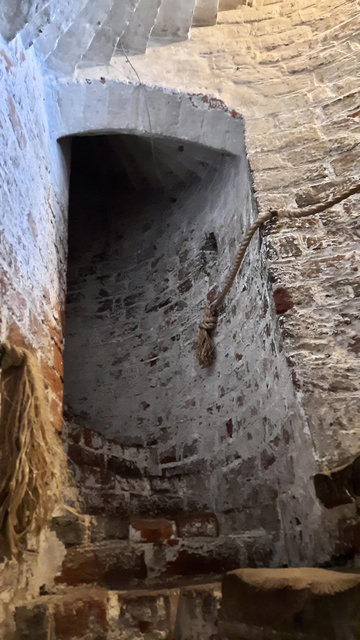 Short version: stone steps. Fuller description: Stone steps and walls curving through a narrow entrance going up to the bell tower in Domkirken, Aarhus cathedral, Denmark. They are worn by use and the centuries, white peeling off to red brick in many places, the steps indented by centuries of footsteps. A worn old rope hangs loosely on the wall as a handrail, fulfilling no health and safety requirements whatsoever.
