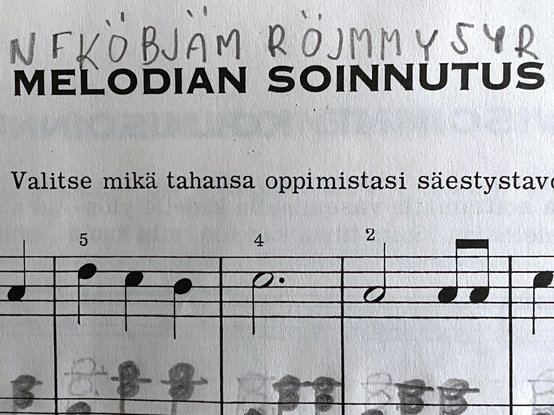 Otsikko "Melodian soinnutus", jonka ylle on lyijykynällä kirjoitettu "NFKÖBJÄM RÖJMMYSYR". Alla ohjetta "Valitse mikä tahansa oppimistasi säestystav", oikean käden melodiaa F-duurissa ja lyijykynällä lisättyjä säestyssointuja.