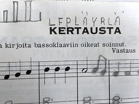 Otsikko "Kertausta" ja sen ylle lyijykynällä tekstattu "LFPLÄYRLÄ". Alla ohjetta "kirjoita bassoklaaviin oikeat soinnut". Nuottiviivaston päällä "Vastaus" ja siitä lähtien painettua melodiaa jatkettu kynällä kirjoittamalla. Vielä vasemmalla ylhäällä loppua tyylitellystä kaunokirjoituksesta "ell".