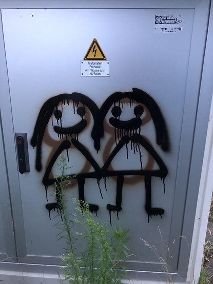 An einem TrafoKasten hat jemand mit brauner Farbe eine 88 angsprüht. Jemand anderes hat mit schwarzer Farbe zwei weiblich gelesene lächelnde Strichmännchen darüber gesprüht, die Händchen halten