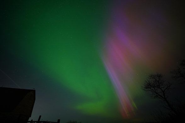 A patch of bright red and purple on one side of the sky, with bright green on the other, looking a bit swirly. There's silhouetted trees in front of the red, and a silhouetted barn in front of the green.