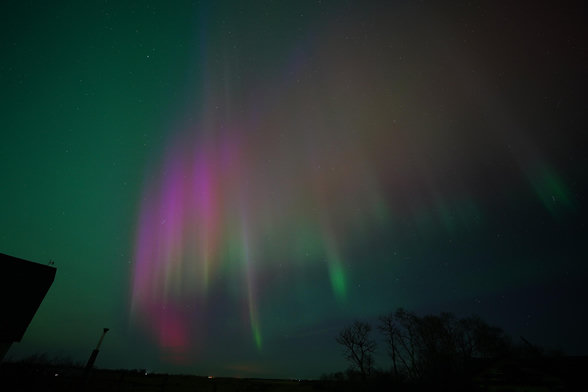 A bunch of columns in an arc, but a few of the columns start lower down in the sky, and are bright green at the bottom. All of the columns transition to orange and then red and the purple. The rest of the sky is green.