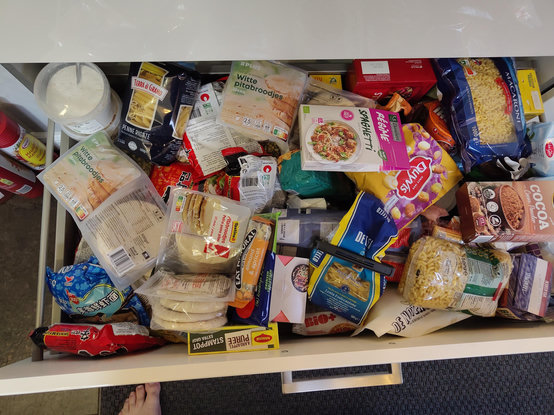 a drawer full of chaotically laid out foods; flatbreads, rice, instant potato powder, cocoa powder, sugar, taco shells, and many many kinds of italian and asian noodles
