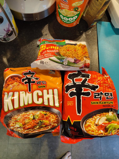 three noodle packets laying on the kitchen counter; Nongshim Shin Kimchi, Nongshim Shin Ramyun, and Indomie Mi Goreng