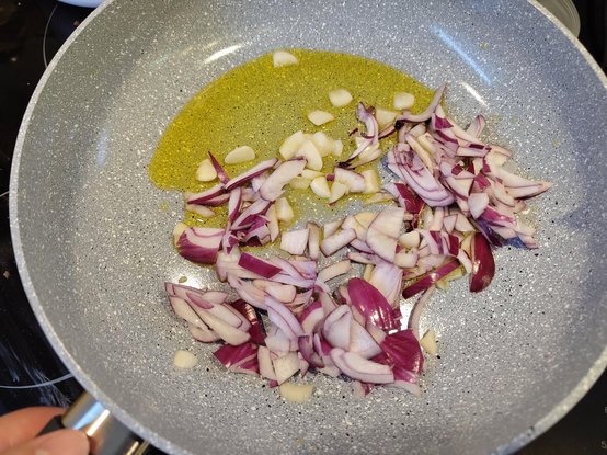 a big ceramic coated frying pan with yellowy oil, chopped garlic, and red onion
