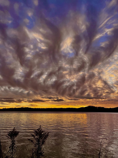 A sunset picture displaying several layers of clouds. At the horizon is a typical orange hue with distant dark bands of clouds. Stretching from the distance to right overhead are dark low clouds with intricate weaving patterns. Above that are white clouds and blue skies. Almost like several photos superimposed, but this is just what that the night presented. Photo from a few years ago.