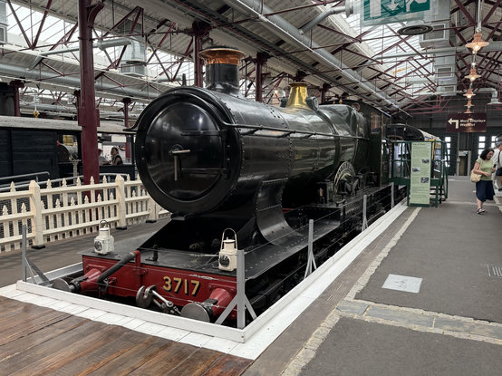 A sleek green steam locomotive with copper chimney and brass bonnet on top of the boiler stood in the former Swindon Machine Shop next to a platform 