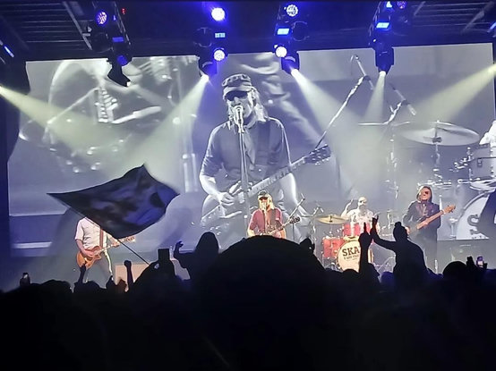 Skay Beilinson y Los Fakires sobre el escenario, detrás una pantalla con un plano sobre Skay y en primer plano la sombra recortada del público 
