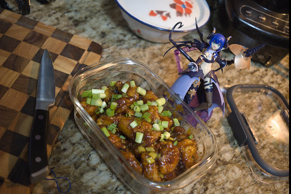 Container of sweet and sour chicken next to an assembled model kit figure of Velretta from Kotobukiya's Arcanadea series.