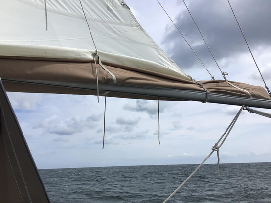 Blick vom Boot auf das Großsegel, Meer im Hintergrund.