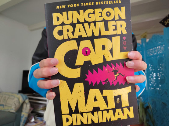 Child holding up Dungeon Crawler Carl by Matt Dinniman.