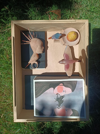 Boîte en bois avec des sculptures, des carnets et des dessins dedans.