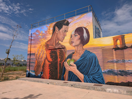A mural in sunset orange tones, the sea in the background, in the foreground two ancient heroes, the man, dressed in red, holding a ball of fire, and the woman, dressed in blue, holding a frog.
Photo: Brad Rubenstein 2026