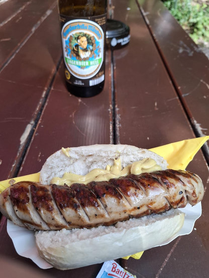 Weiße Bratwurst in der Semmel an auge grün auf biergartentisch