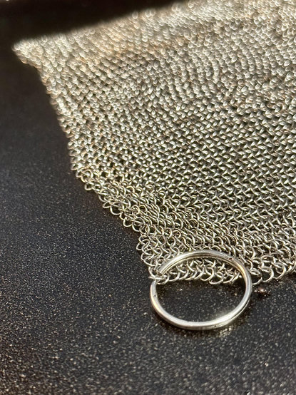 As an artist I just can’t not notice how the texture and mesh pattern of the miniature chain links are fascinating. The vey close view here is a good detail view of the mesh cleaning cloth from the ring at the corner to hang it up for storing it. I’m proud of the nice cleaning I did on an old pan seasoned right with oil. 