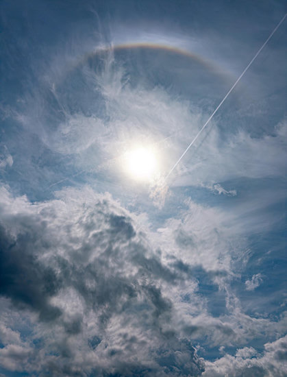 Another picture of the Sun in a partly cloudy sky, this time showing just the bright and colourful upper part of the 22º halo, along with a diagonal contrail and its shadow.