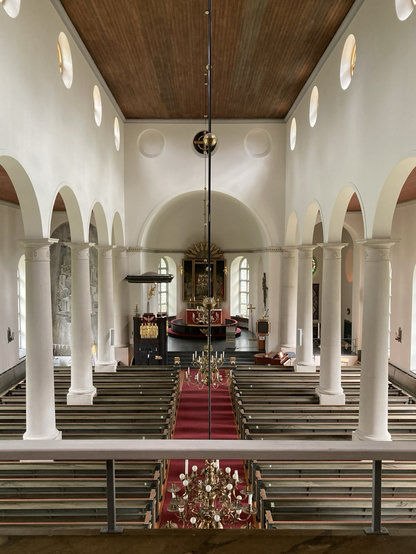 Bild av Åsele kyrka med stora vita pelare på respektive sida om kyrkgången. Längst fram i den stora kyrkan skymtar altaret med det röda antipendiet.