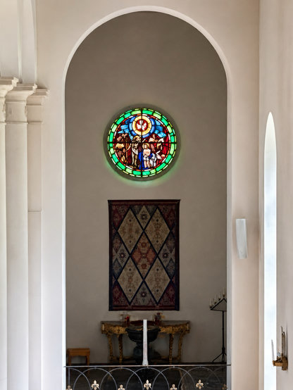 Ett vitt dopkor med ett färgglatt kyrkfönster.