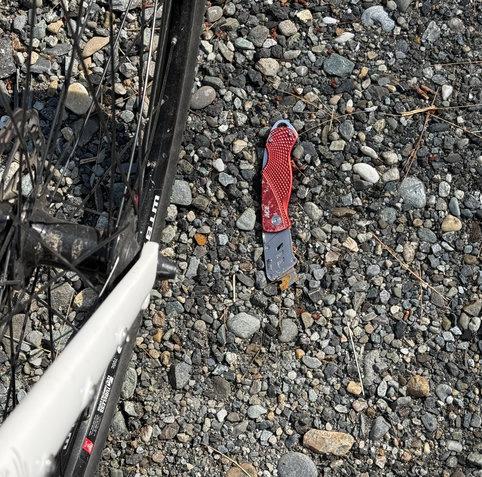 A red aluminum folding sheet rock knife with broken blade laying in the gravel.