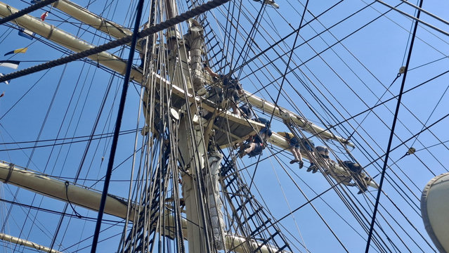 Short version: Sailors on masts. Fuller descriptions: Young sailors dotted around high up on the ropes and riggings and masts of a ship, working on the sails while moored at the Tall Ships Race in Aarhus Denmark (last week). Deep bright blue sky.