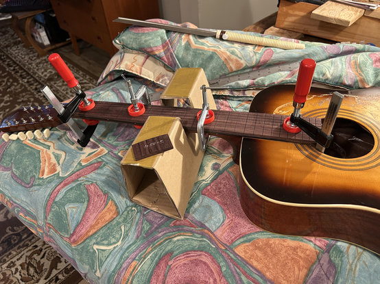 it’s the project guitar, an old Framus 12 string acoustic, stripped, with a new rosewood fretboard clamped into place, on a colourful green blanket. Somebody wrote, "loser," on one end of the new fretboard, so I cuth that part off. ;)