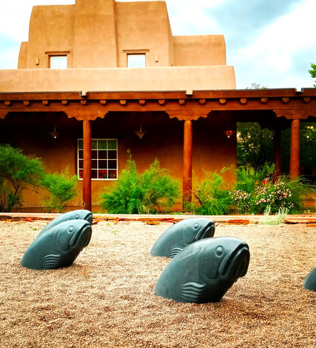 a sculpture of fish emerging from the ground in front of an adobe building