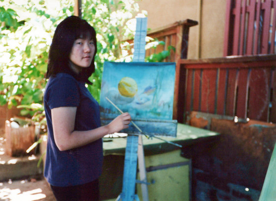 An old photo of Joy painting on an easel outside.