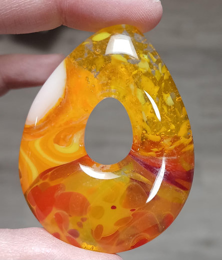 teardrop shaped pendant with a mix of yellows with accents of orange, red white and clear. its got a lot of movement in it, you can tell it's an ex-liquid.