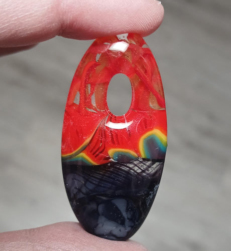 an oval pendant with swirling, ribbonlike red in clear on top and purples on the bottom