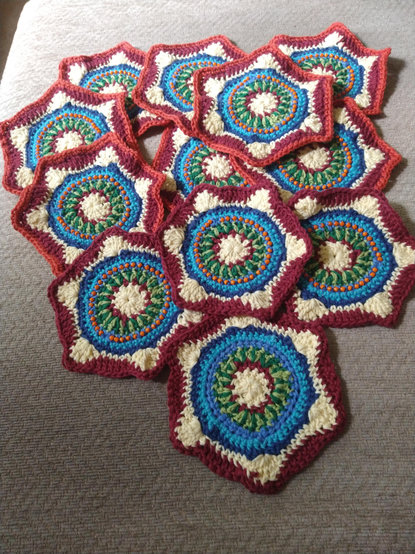 Twelve hexagonal crochet motifs with a white and burgundy centre, and a ring of two tone green, then blue with orange bead detail