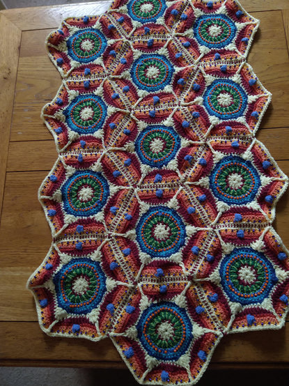 Twelve hexagonal crochet motifs with a white and burgundy centre, and a ring of two tone green, then blue with orange bead detail, all pieces have a white border and are pieced together giving a rectangular shape!