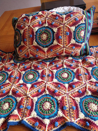 Part of Multi coloured Crochet piece laid on a dining table at the top is a cushion in the same pattern