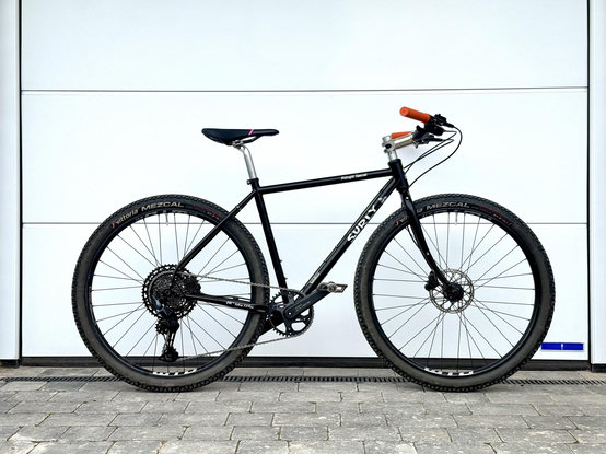 A black Surly Midnight Special flat bar build stood against a white garage door. Because them's the rules.