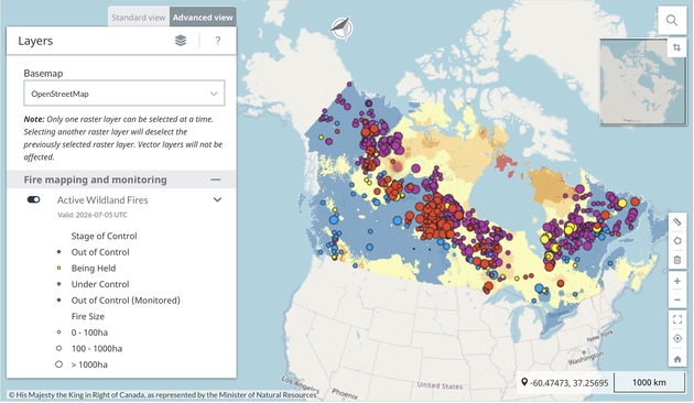 Image description (accessible version):

The image is a screenshot of an interactive Canadian wildfire monitoring map displayed in a web browser. The interface consists of a large map on the right and a control panel on the left.

The map shows nearly all of Canada covered with hundreds of colored circles of varying sizes, each representing an active wildfire. The colors indicate the fire’s status:

* Red: Out of control
* Yellow: Being held
* Blue: Under control
* Purple: Out of control (monitored)

The size of each circle represents the fire’s estimated area:

* Small: 0–100 hectares
* Medium: 100–1,000 hectares
* Large: More than 1,000 hectares

Wildfires are concentrated across northern and central Canada. Large clusters of red and purple circles are visible in the Northwest Territories, northern Alberta and Saskatchewan, around Hudson Bay, and across parts of Québec and Labrador. Southern Canada, particularly along the U.S. border, has noticeably fewer wildfire markers.

The map background is shaded in different colors, including blue, pale yellow, orange, and red, indicating an additional thematic layer. However, the screenshot does not provide a legend explaining what these background colors represent.

The left-hand panel is titled “Layers” and is shown in Advanced View. The selected basemap is OpenStreetMap, and the Active Wildland Fires layer is enabled. The data are marked as valid for 5 July 2026 (UTC). The panel also includes a legend explaining the wildfire status colors and circle sizes.

On the right side of the screen are standard map controls, including search, zoom, fullscreen, and navigation tools. A small overview map appears in the upper-right corner, and a scale bar in the lower-right corner indicates a distance of 1,000 km.