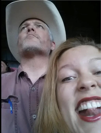 A middle aged man and a young woman, shot from below. He's in a cowboy hat, looking into the distance like the Marlboro Man without the lung cancer. She's making a happy goofy face at the camera.